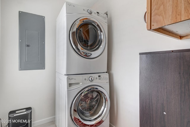 laundry area with stacked washer / drying machine, cabinets, and electric panel