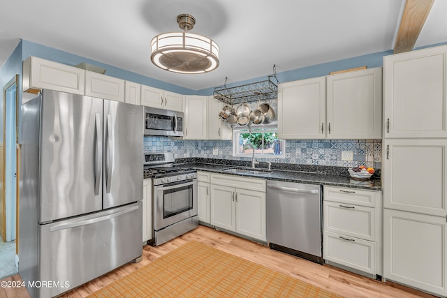 kitchen featuring white cabinets, appliances with stainless steel finishes, dark stone counters, light hardwood / wood-style floors, and sink