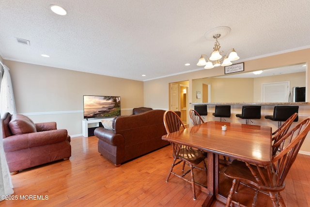 dining area with a chandelier, light hardwood / wood-style floors, and a textured ceiling