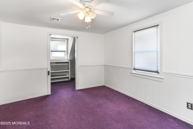 empty room with ceiling fan and dark colored carpet