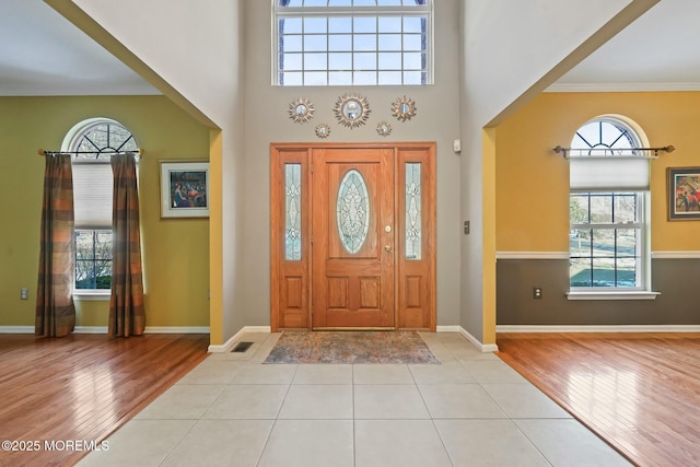 foyer entrance featuring a high ceiling, ornamental molding, and light wood-type flooring