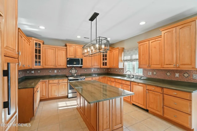 kitchen with light tile patterned flooring, a kitchen island, appliances with stainless steel finishes, sink, and hanging light fixtures