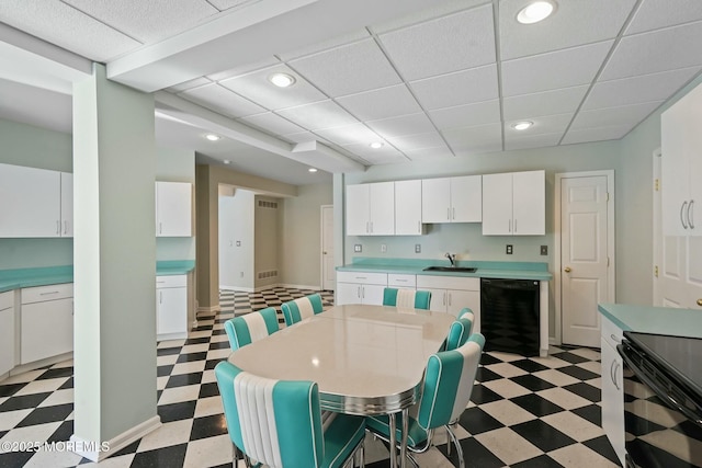 kitchen with sink, white cabinetry, a kitchen breakfast bar, black dishwasher, and a drop ceiling