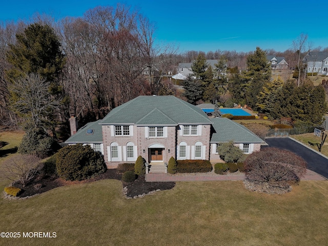 colonial-style house with aphalt driveway, a chimney, and a front lawn