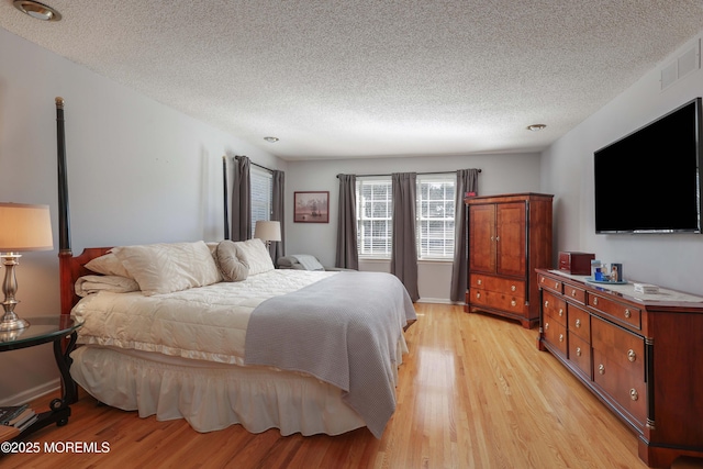 bedroom with light wood finished floors, baseboards, visible vents, and a textured ceiling