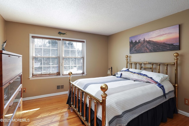 bedroom featuring a textured ceiling, light wood finished floors, visible vents, and baseboards