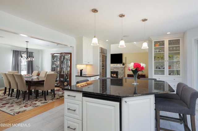 kitchen with dark stone counters, a stone fireplace, a kitchen island, and white cabinets