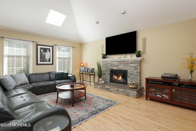 living area with light wood finished floors, vaulted ceiling with skylight, and a stone fireplace