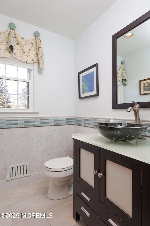 bathroom featuring tile walls, visible vents, toilet, vanity, and tile patterned floors