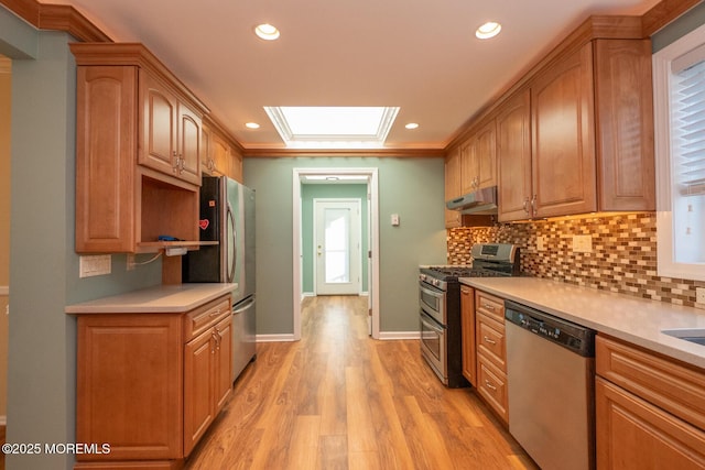 kitchen featuring crown molding, appliances with stainless steel finishes, a skylight, light hardwood / wood-style floors, and decorative backsplash