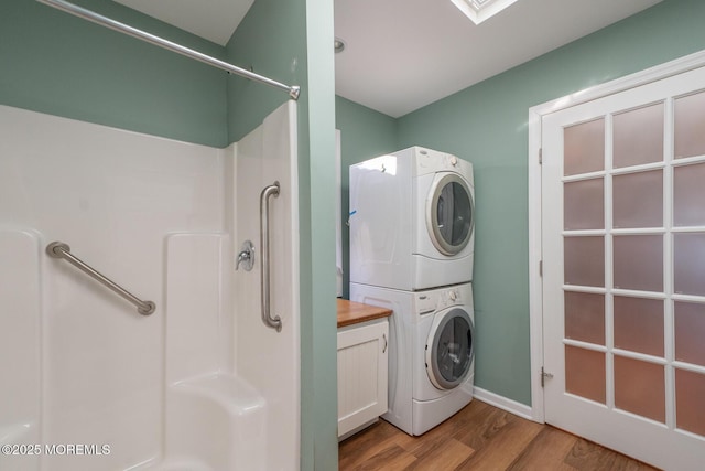 laundry room with stacked washer / drying machine and light hardwood / wood-style flooring