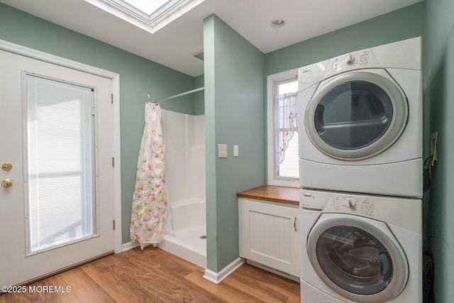 clothes washing area featuring a skylight, light wood-type flooring, and stacked washer / dryer