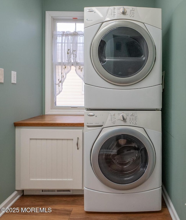 clothes washing area featuring cabinets, stacked washer and dryer, and light hardwood / wood-style flooring