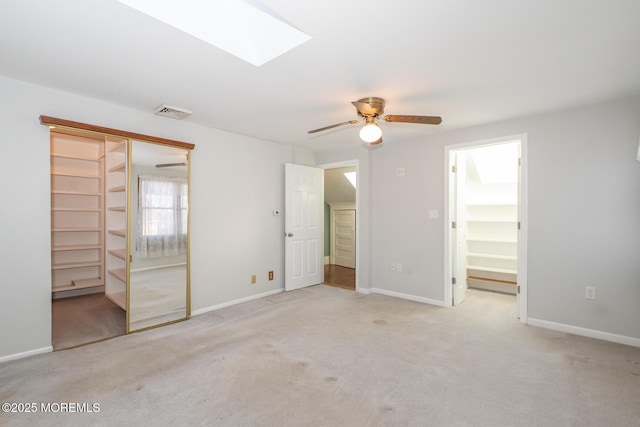 unfurnished bedroom featuring a closet, light colored carpet, ceiling fan, and a skylight