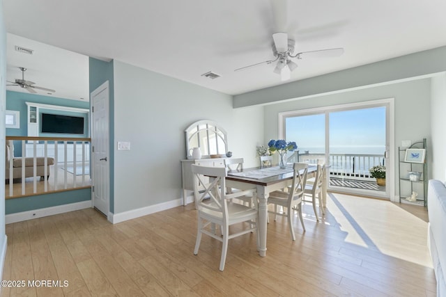 dining space with light wood-type flooring, ceiling fan, and a water view