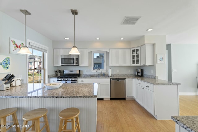 kitchen with white cabinets, hanging light fixtures, light hardwood / wood-style floors, kitchen peninsula, and stainless steel appliances