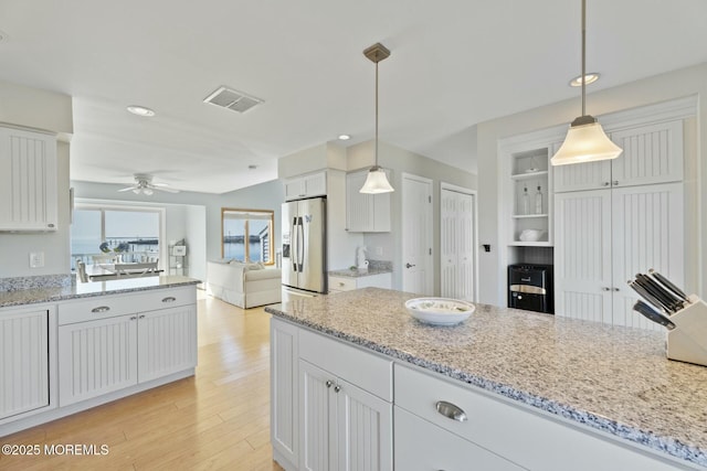 kitchen featuring hanging light fixtures, white cabinetry, stainless steel fridge, and light stone counters