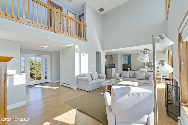 living room featuring a baseboard radiator, light wood-type flooring, and a towering ceiling