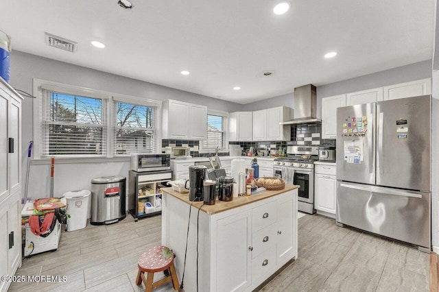 kitchen featuring a center island, white cabinetry, decorative backsplash, wall chimney range hood, and stainless steel appliances