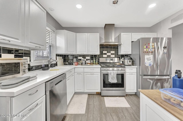 kitchen featuring white cabinetry, decorative backsplash, wall chimney range hood, light hardwood / wood-style flooring, and stainless steel appliances