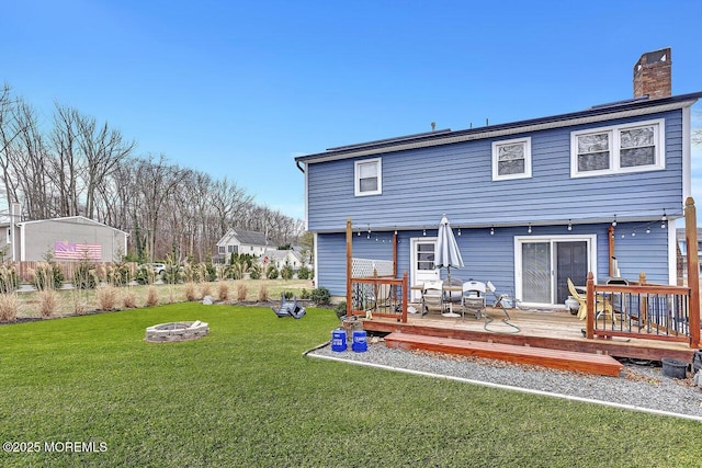 rear view of property featuring a deck, a lawn, and a fire pit