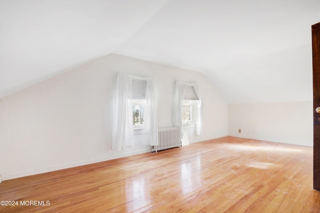 additional living space with radiator heating unit, light hardwood / wood-style flooring, and vaulted ceiling