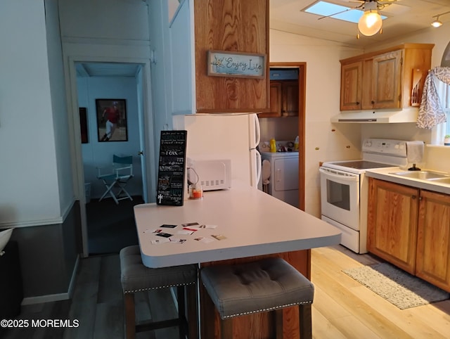 kitchen with washing machine and clothes dryer, light countertops, white appliances, light wood-style floors, and a kitchen breakfast bar
