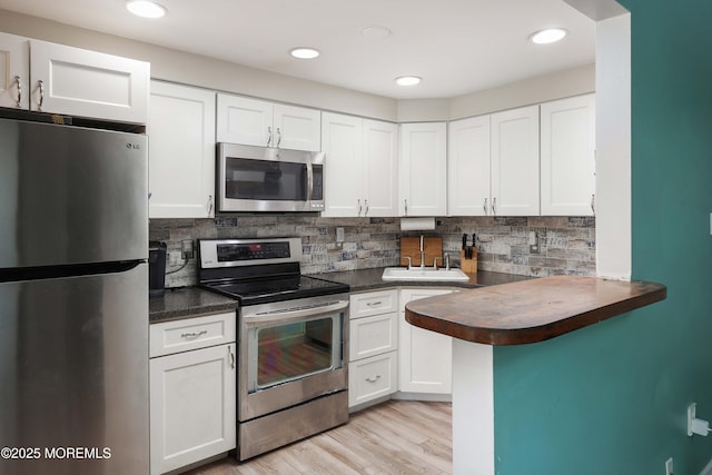 kitchen with appliances with stainless steel finishes, sink, white cabinets, decorative backsplash, and kitchen peninsula