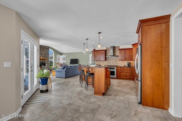 kitchen featuring a kitchen island, wall chimney range hood, stainless steel appliances, a kitchen breakfast bar, and vaulted ceiling