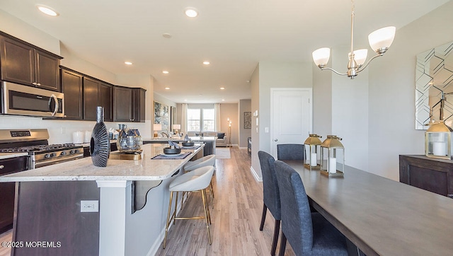 kitchen with pendant lighting, a breakfast bar area, appliances with stainless steel finishes, dark brown cabinetry, and an island with sink