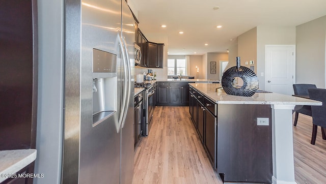 kitchen with a breakfast bar area, appliances with stainless steel finishes, a center island, light stone countertops, and light wood-type flooring