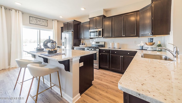 kitchen featuring light stone counters, stainless steel appliances, sink, and light wood-type flooring