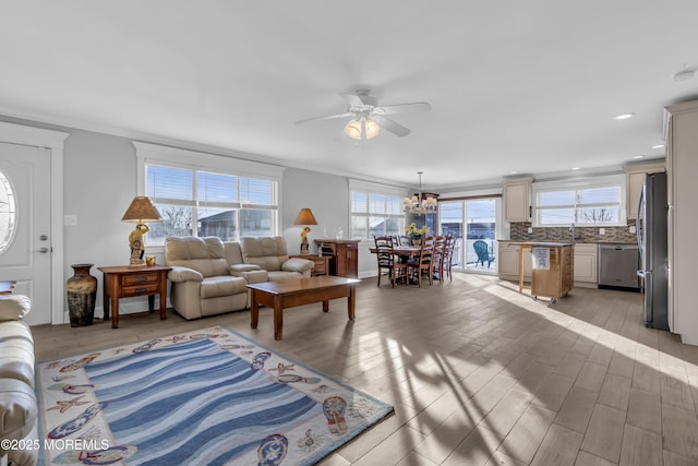 living room featuring crown molding, ceiling fan with notable chandelier, and light hardwood / wood-style floors