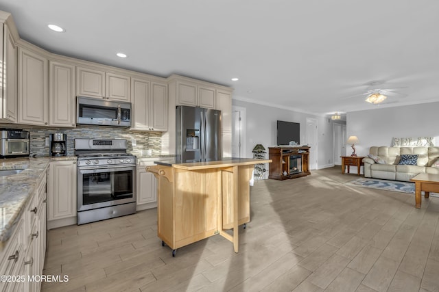 kitchen featuring appliances with stainless steel finishes, cream cabinets, backsplash, a kitchen bar, and light stone countertops