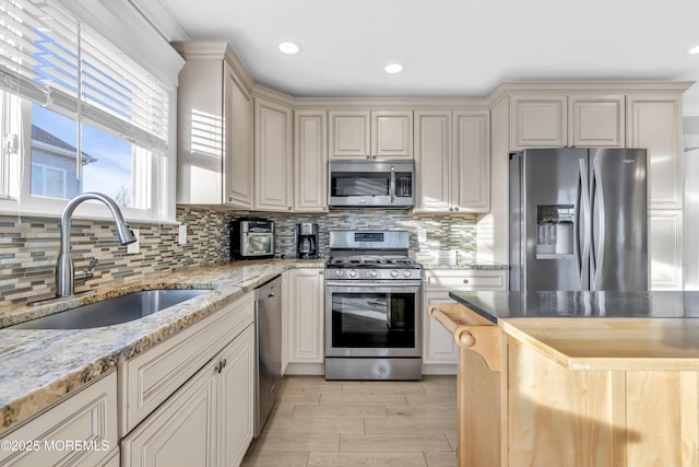 kitchen with appliances with stainless steel finishes, cream cabinets, sink, decorative backsplash, and light stone countertops