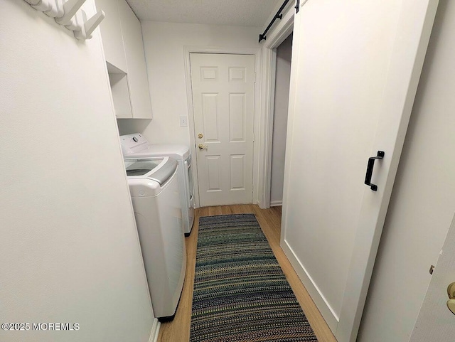 clothes washing area featuring washing machine and dryer, a barn door, light hardwood / wood-style flooring, and cabinets