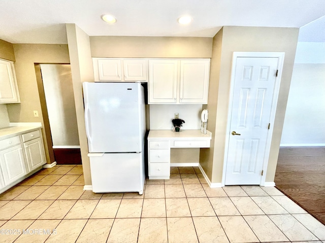 kitchen with white cabinetry, white fridge, built in desk, and light tile patterned floors