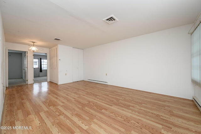 spare room featuring a baseboard heating unit and light hardwood / wood-style floors