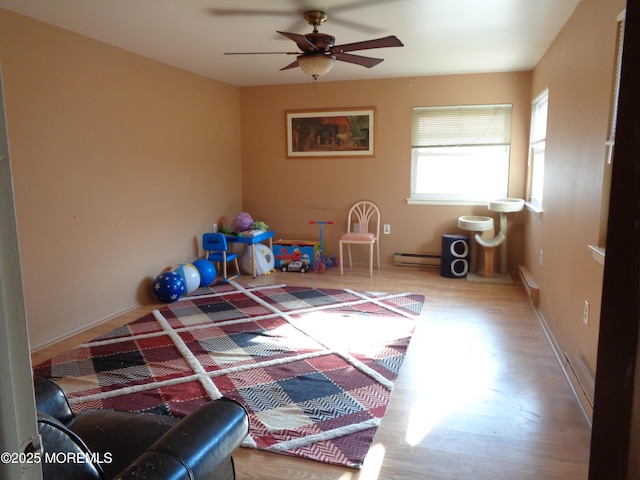 recreation room featuring a baseboard radiator, wood-type flooring, and ceiling fan