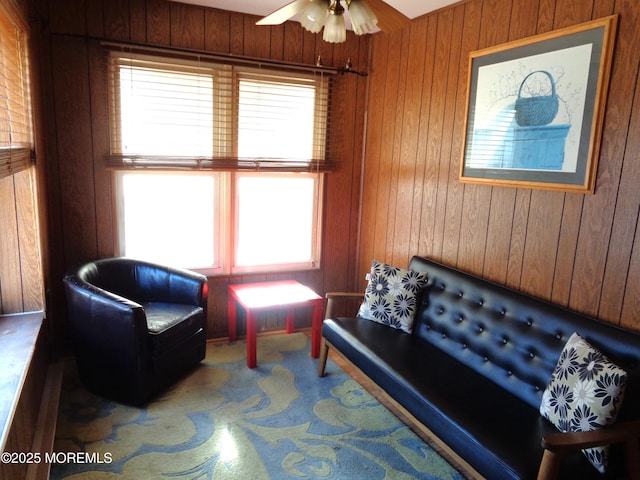 sitting room with ceiling fan, carpet flooring, and wood walls