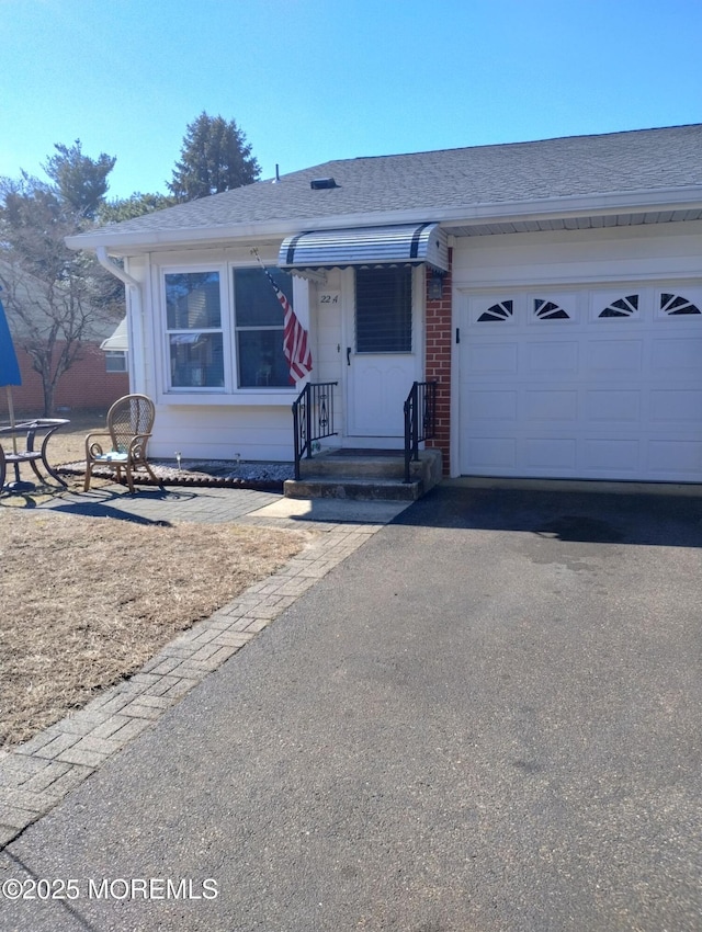 view of front facade featuring a garage, brick siding, aphalt driveway, and roof with shingles