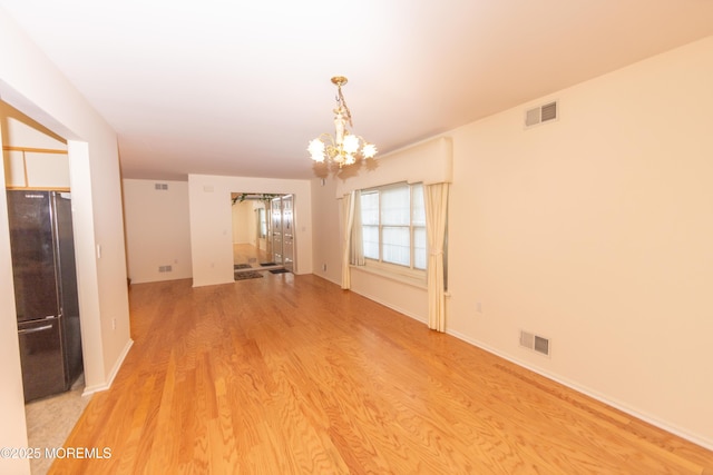 spare room with light wood-style floors, visible vents, and a chandelier