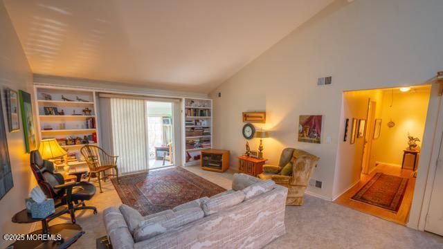 living area featuring high vaulted ceiling, built in shelves, carpet flooring, and visible vents