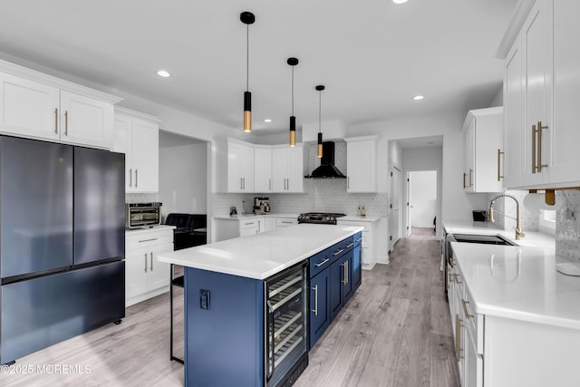 kitchen featuring blue cabinetry, white cabinetry, wine cooler, black fridge, and wall chimney exhaust hood