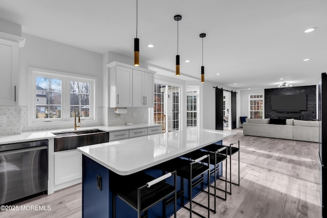 kitchen featuring sink, white cabinetry, a center island, stainless steel dishwasher, and a barn door