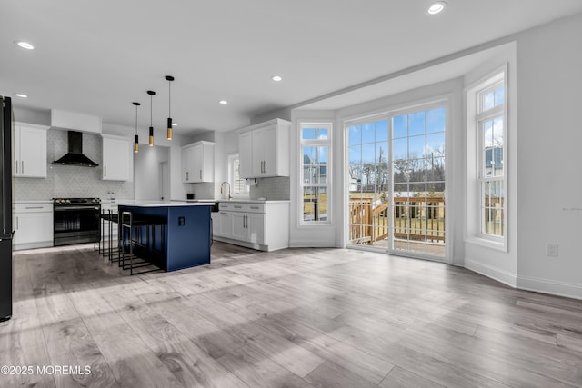 kitchen with wall chimney exhaust hood, white cabinetry, a center island, hanging light fixtures, and stainless steel stove