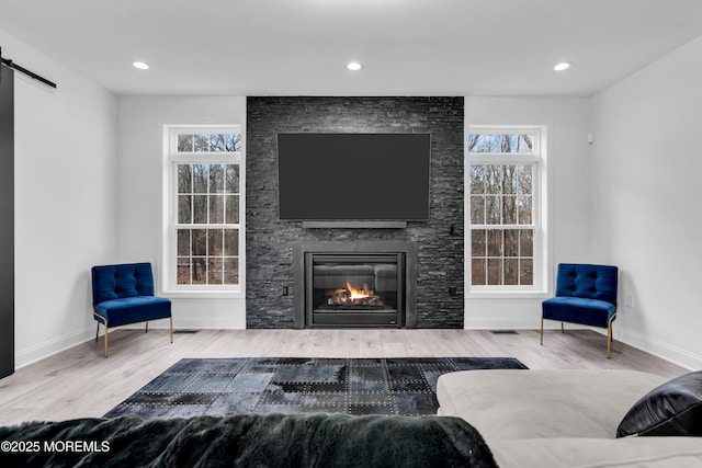 living room featuring wood-type flooring, a barn door, and a stone fireplace