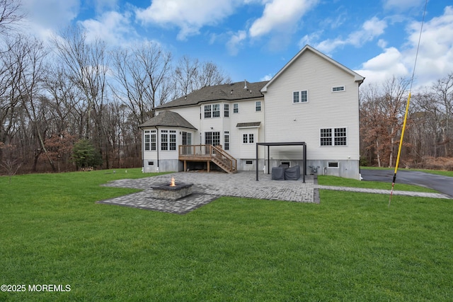 rear view of house featuring a lawn, a patio, an outdoor fire pit, a wooden deck, and a sunroom