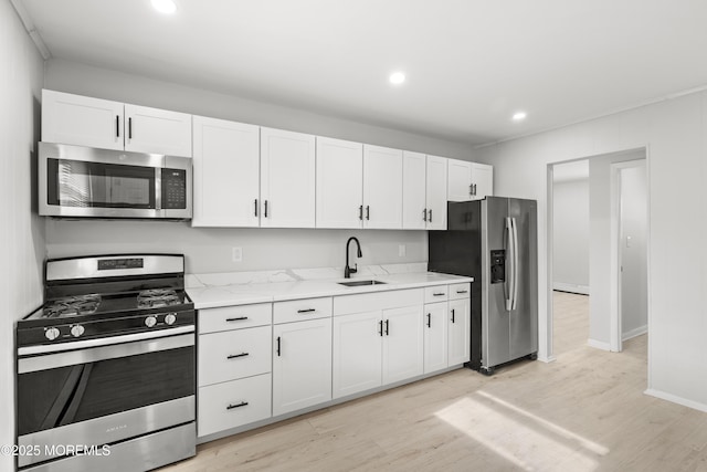 kitchen featuring stainless steel appliances, white cabinetry, light stone countertops, and sink