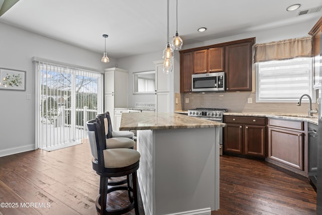 kitchen with sink, light stone counters, appliances with stainless steel finishes, a kitchen island, and decorative backsplash